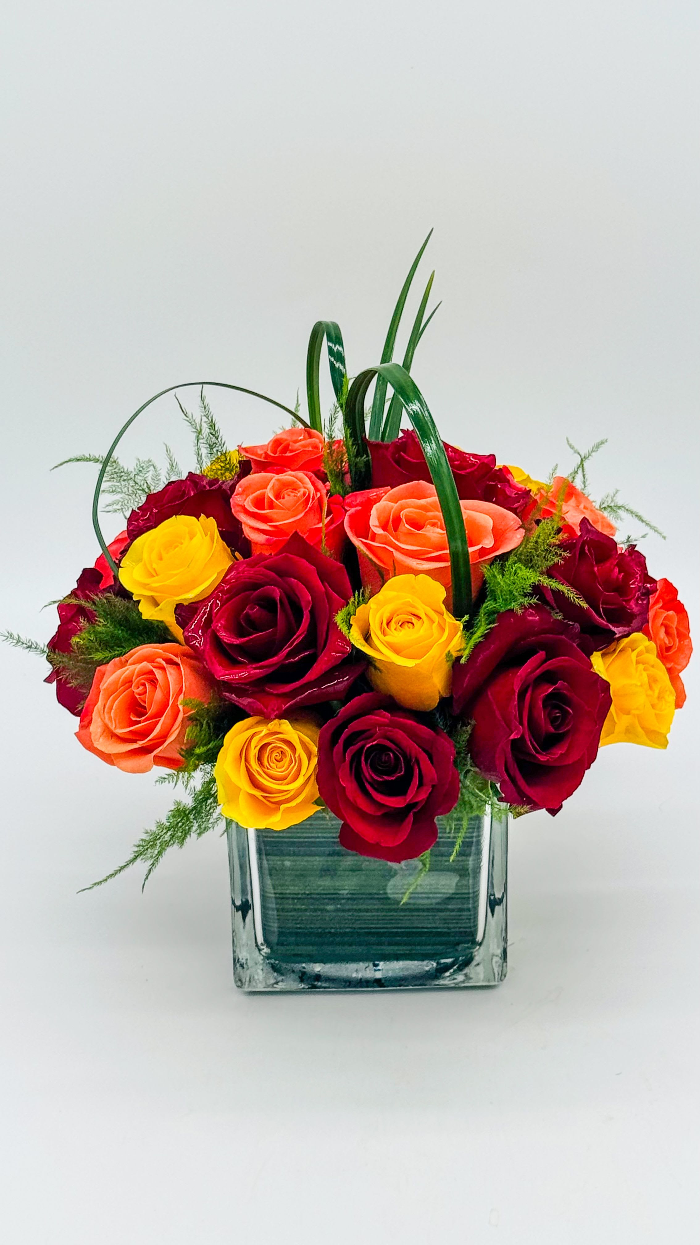 Bouquet of red, yellow, and orange roses in a square glass vase