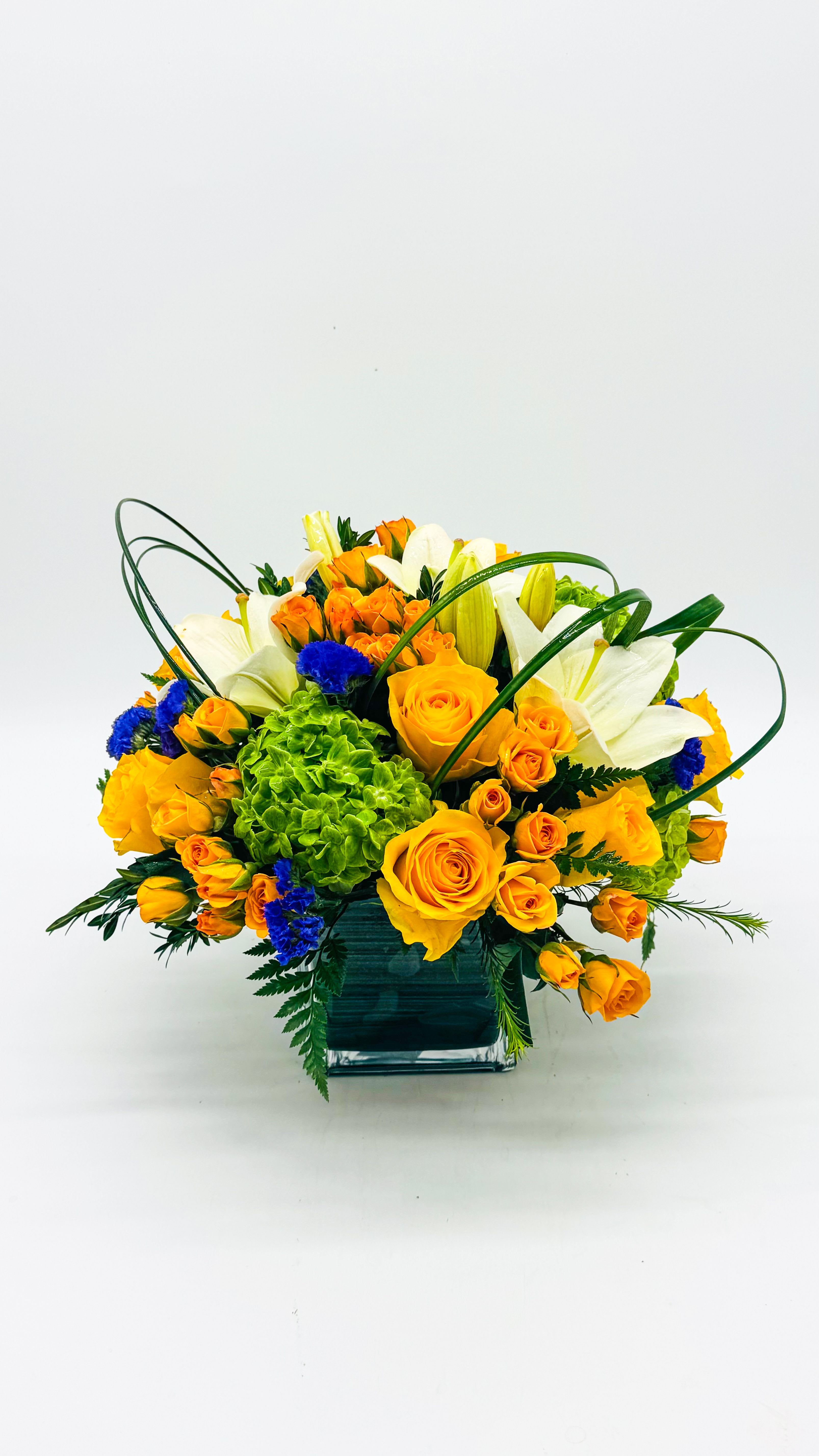Orange roses and white lilies in a square glass vase