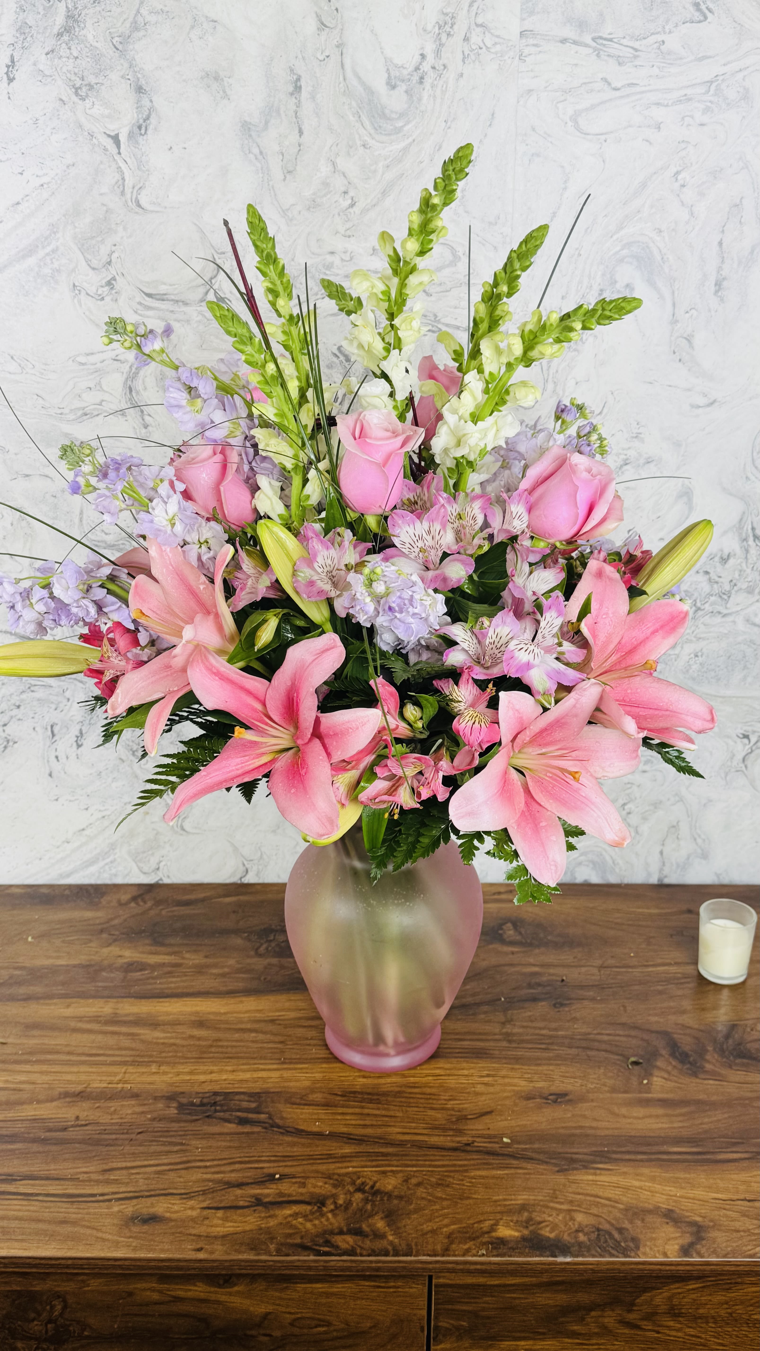 Pink lilies and roses arranged in a frosted glass vase