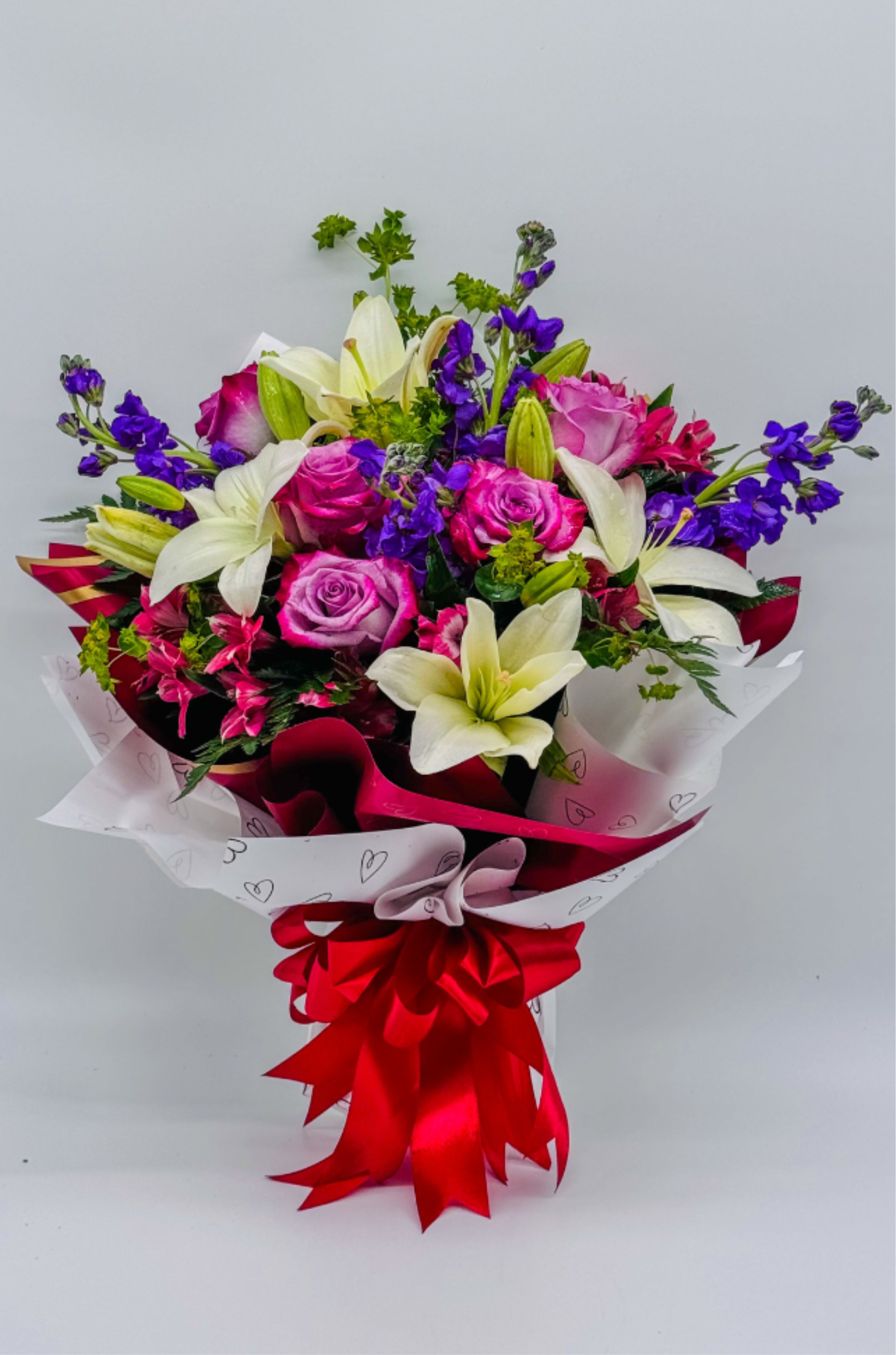 Eternal Amour - Classic romantic bouquet featuring purple roses and white lilies, accented with purple stock  Green foliage adds fullness. In the vase and water to stay long time fresh Wrapped in white and pink layers with a bold red ribbon. Elegant, compact arrangement with a soft, feminine feel. Perfect for anniversary, birthday, Father's Day, get well, graduations or just because thank you , I'm sorry , Mother's Day,Valentine's Day