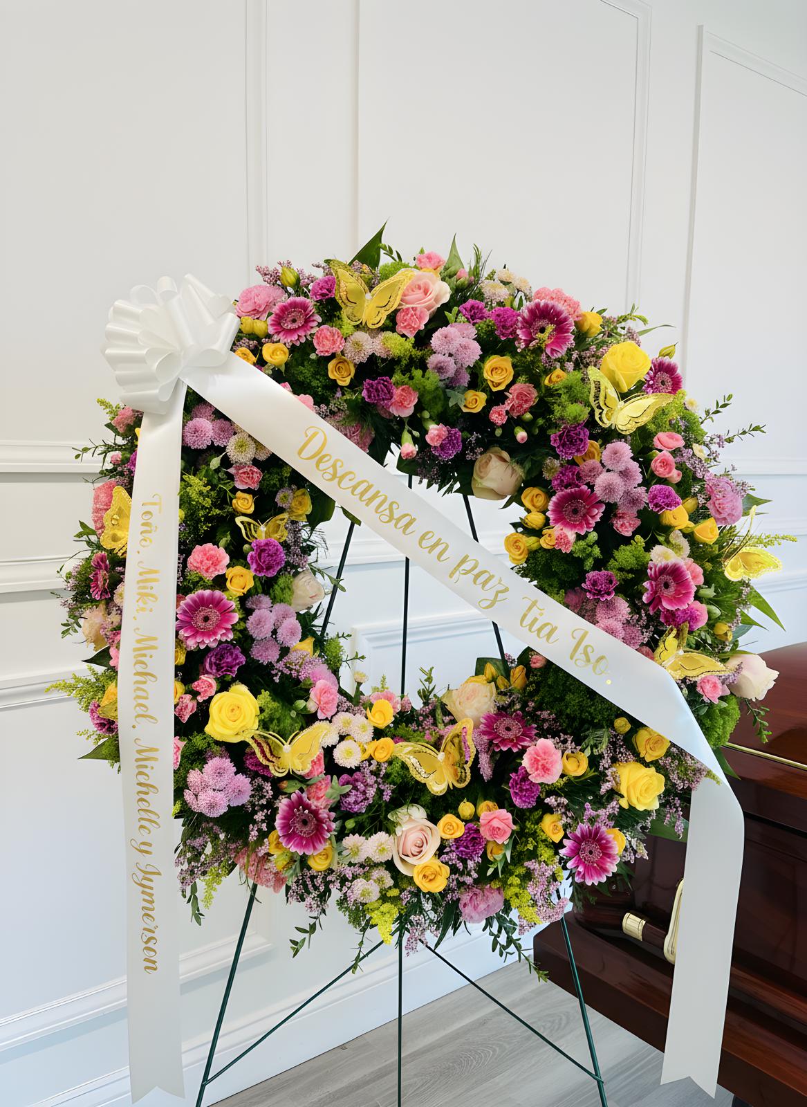 Large floral wreath with pink, yellow, and purple blooms on a stand with white ribbons