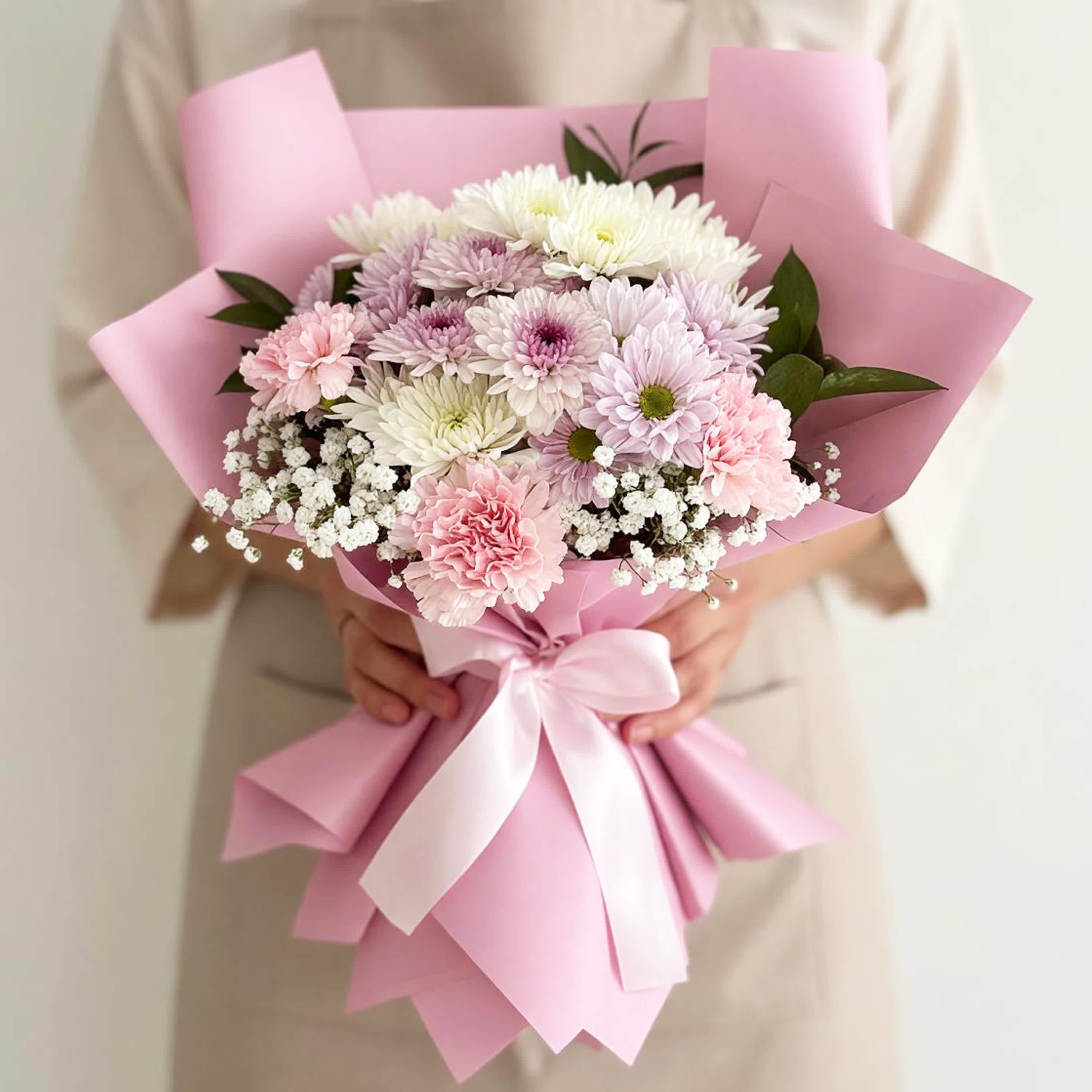 Pink-wrapped bouquet of pastel chrysanthemums with a white ribbon