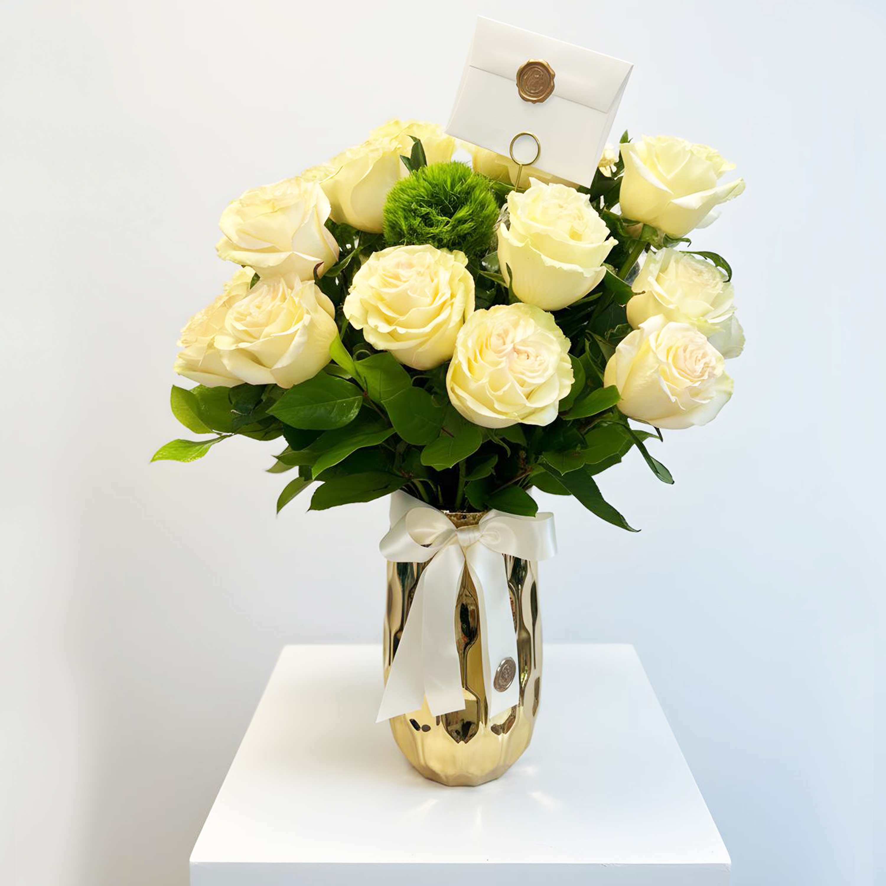 White roses in a gold vase with a ribbon and card holder.