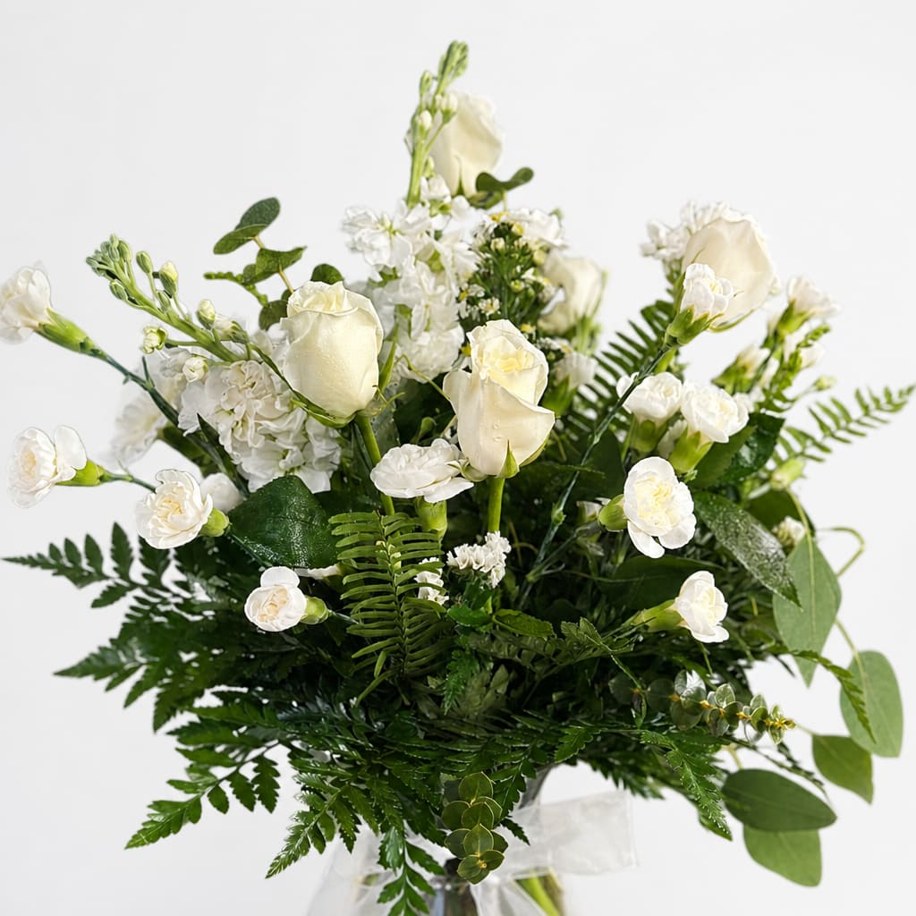 White roses and small white flowers in a clear vase with greenery