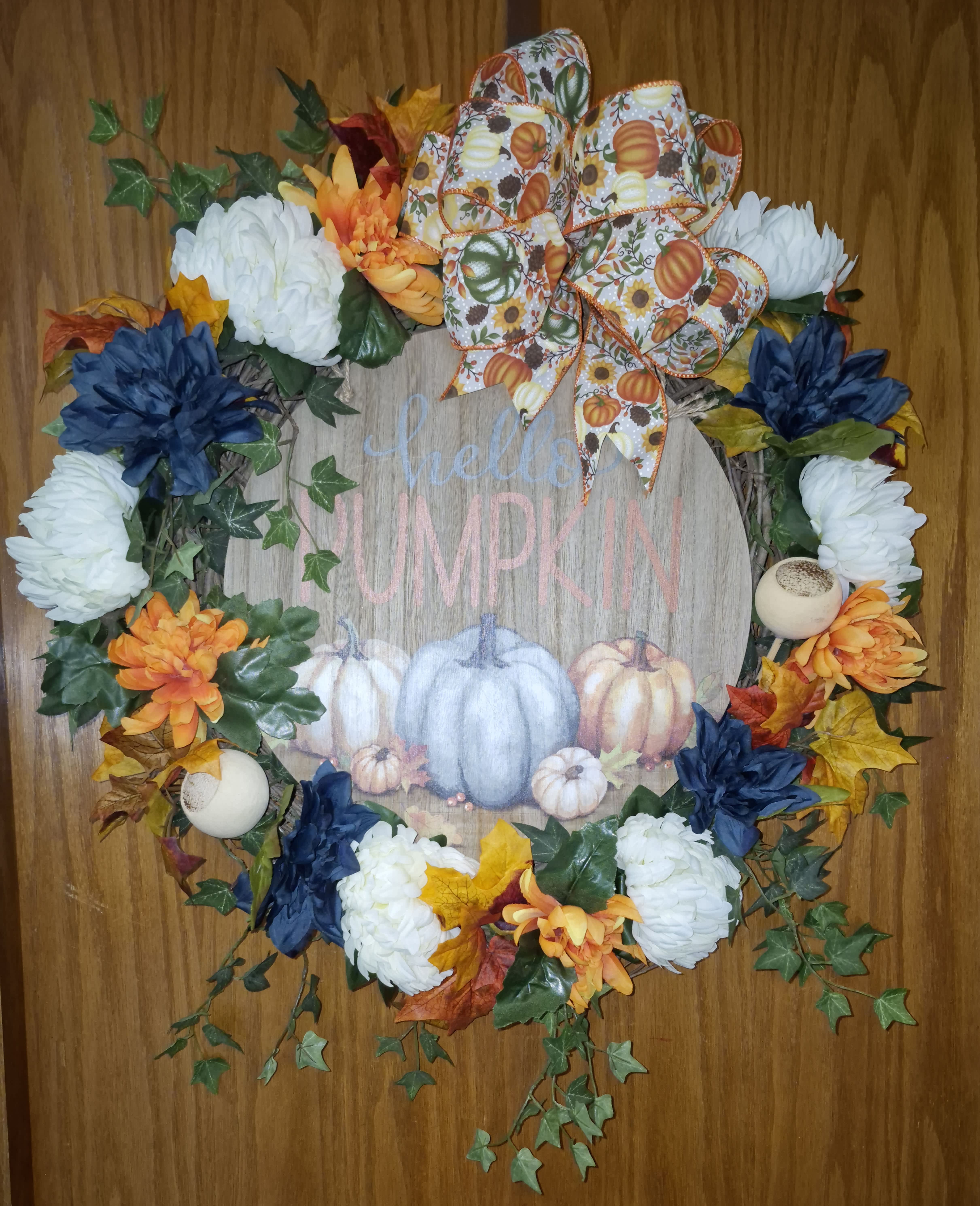 Fall wreath with white and orange flowers, blue accents, and a pumpkin ribbon