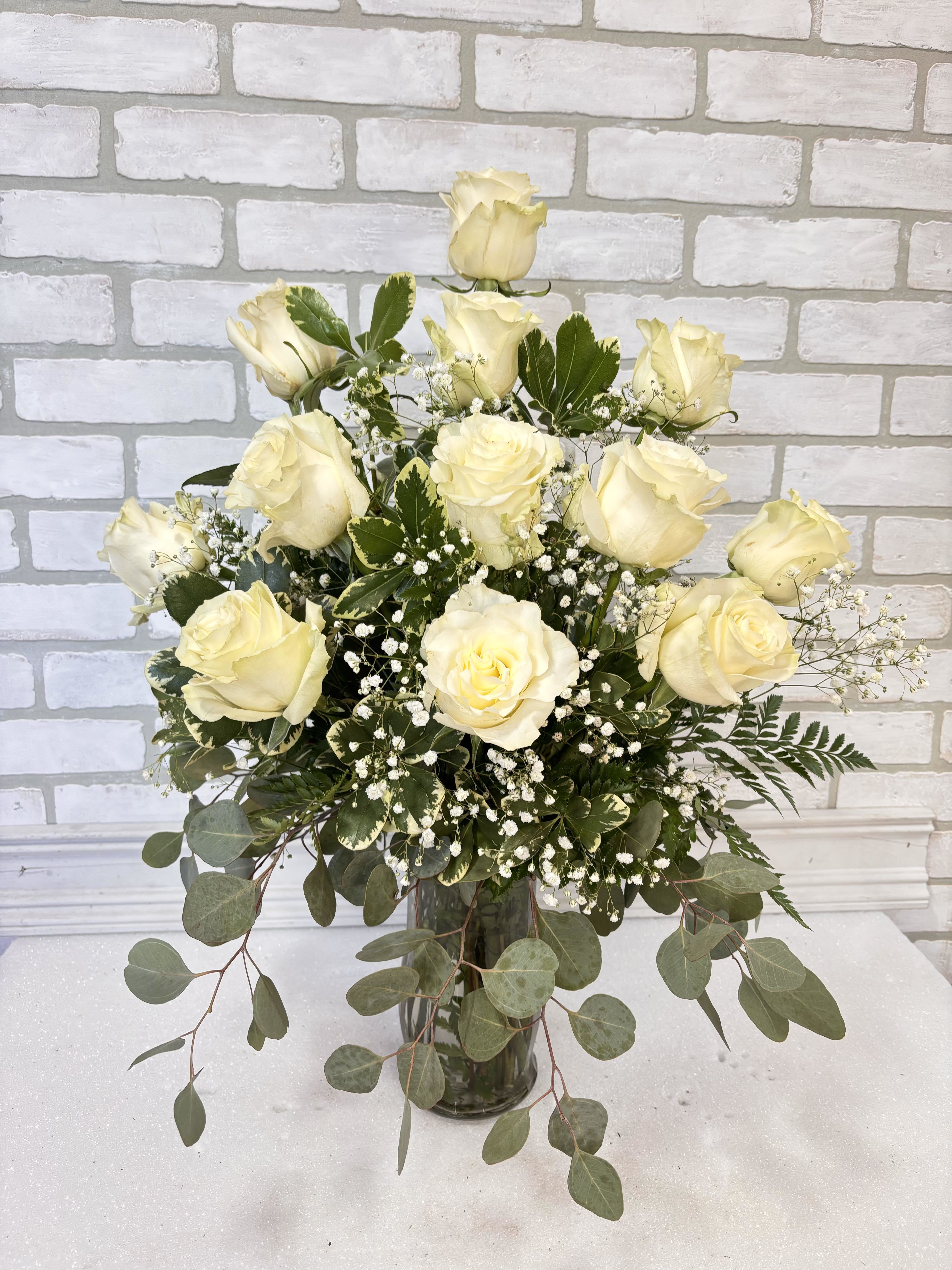 Tall arrangement of white roses and baby's breath in a clear glass vase with cascading eucalyptus