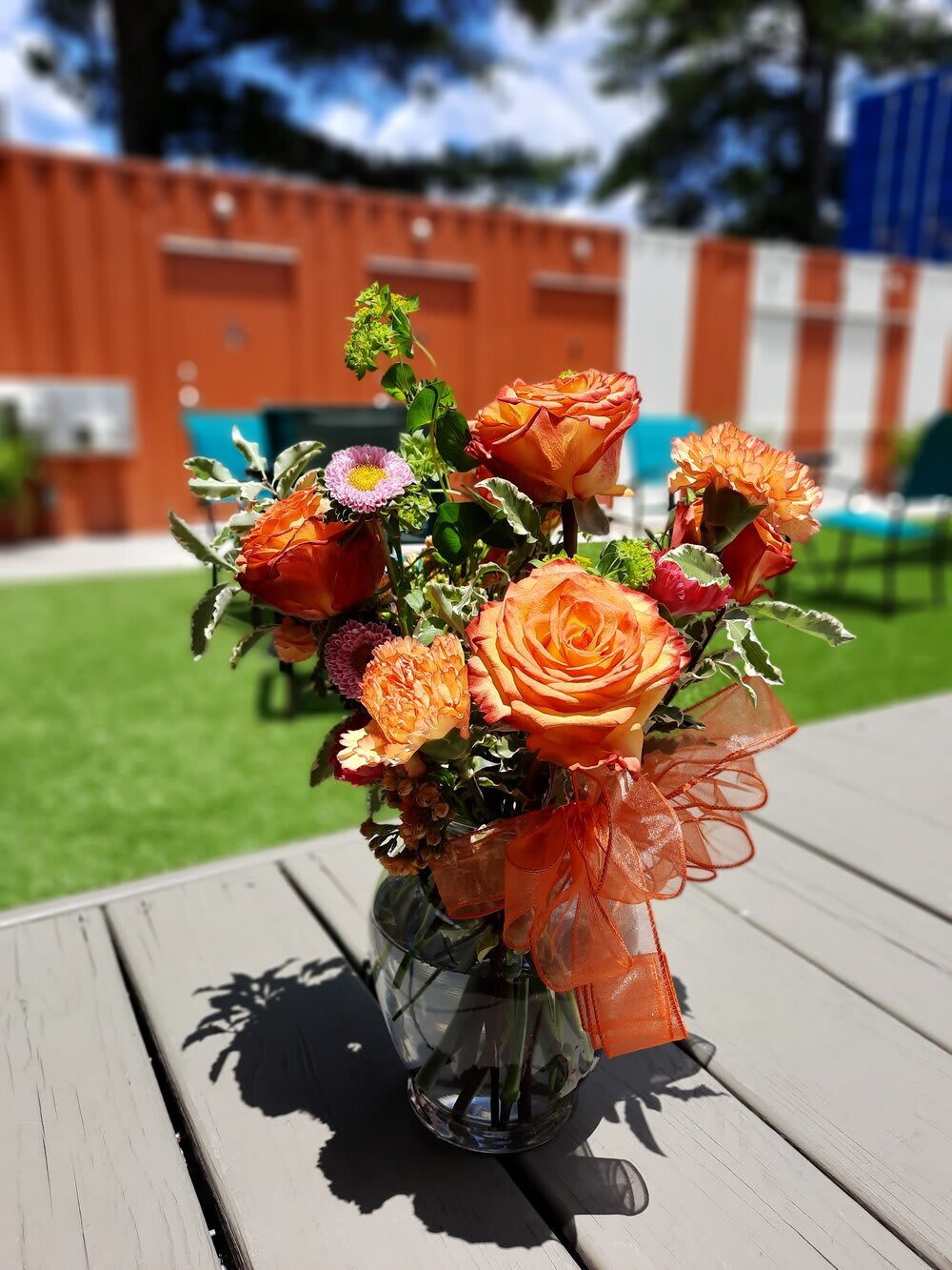 Orange rose bouquet in a glass vase with an orange ribbon