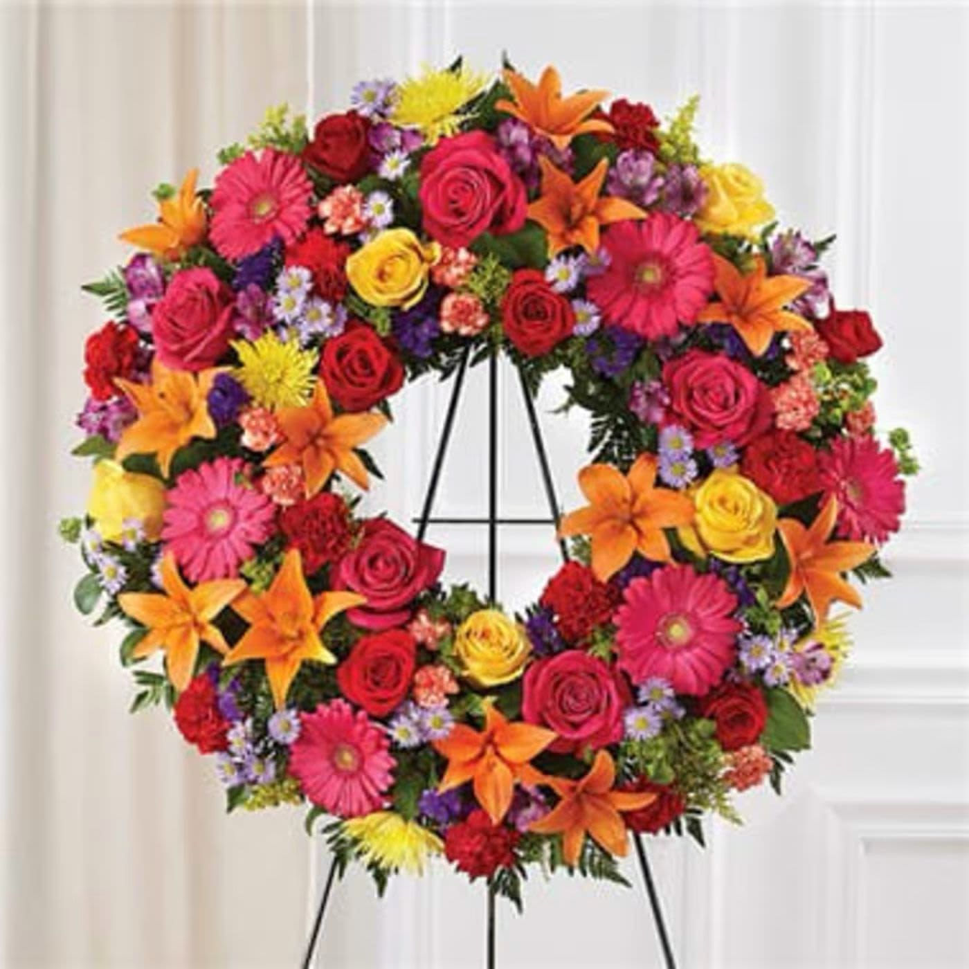 Colorful floral wreath on a stand with roses, lilies, and daisies