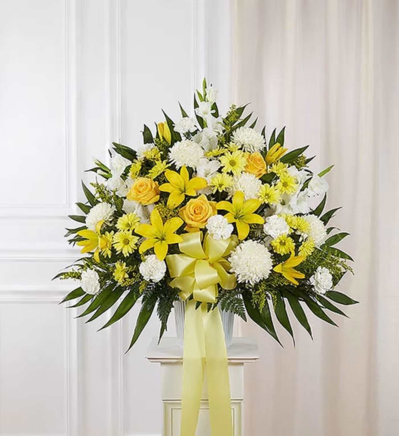 Yellow and white floral arrangement with a ribbon in a clear vase