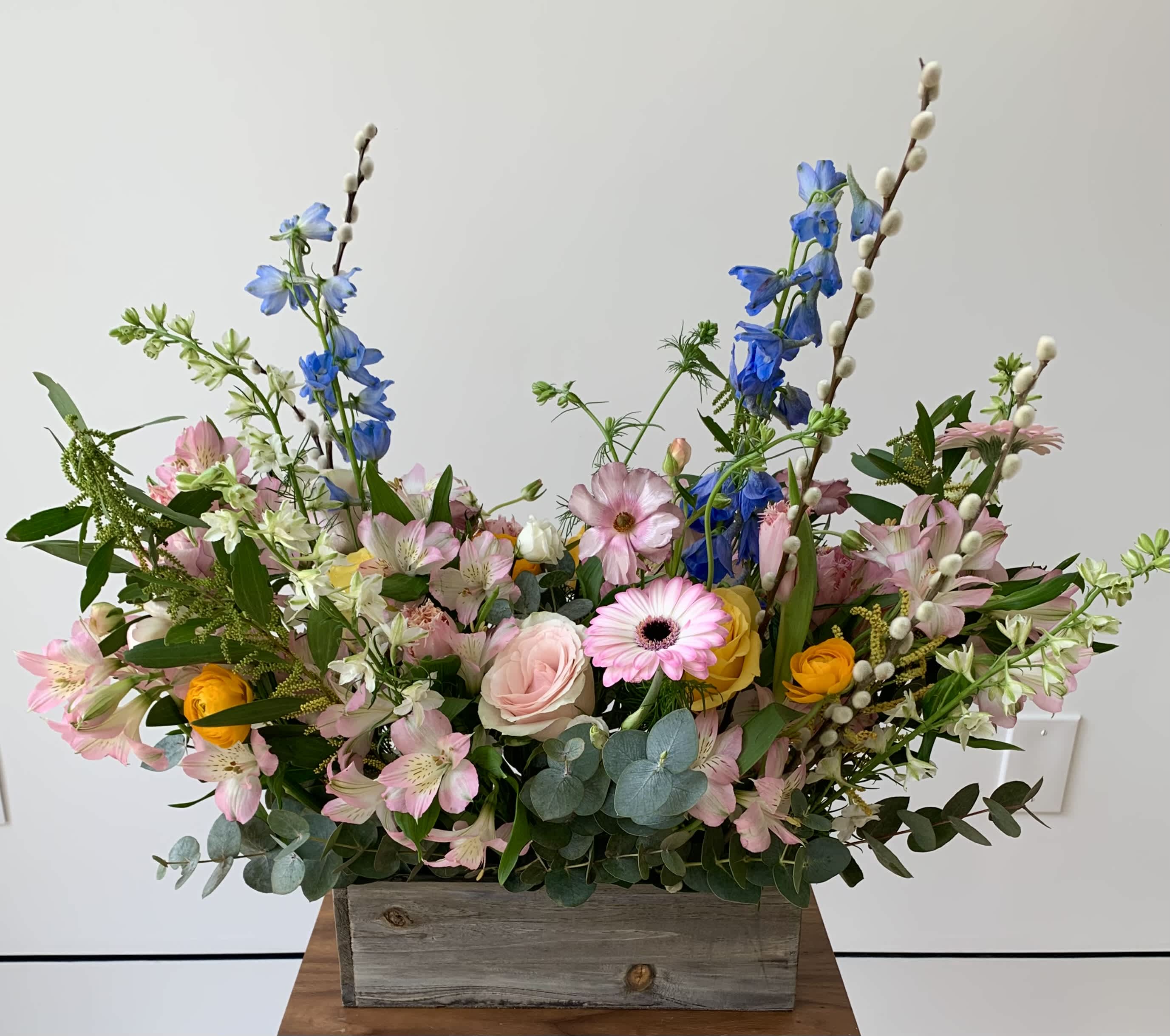 Mixed bouquet in a rustic wooden box with pink, blue, and yellow flowers