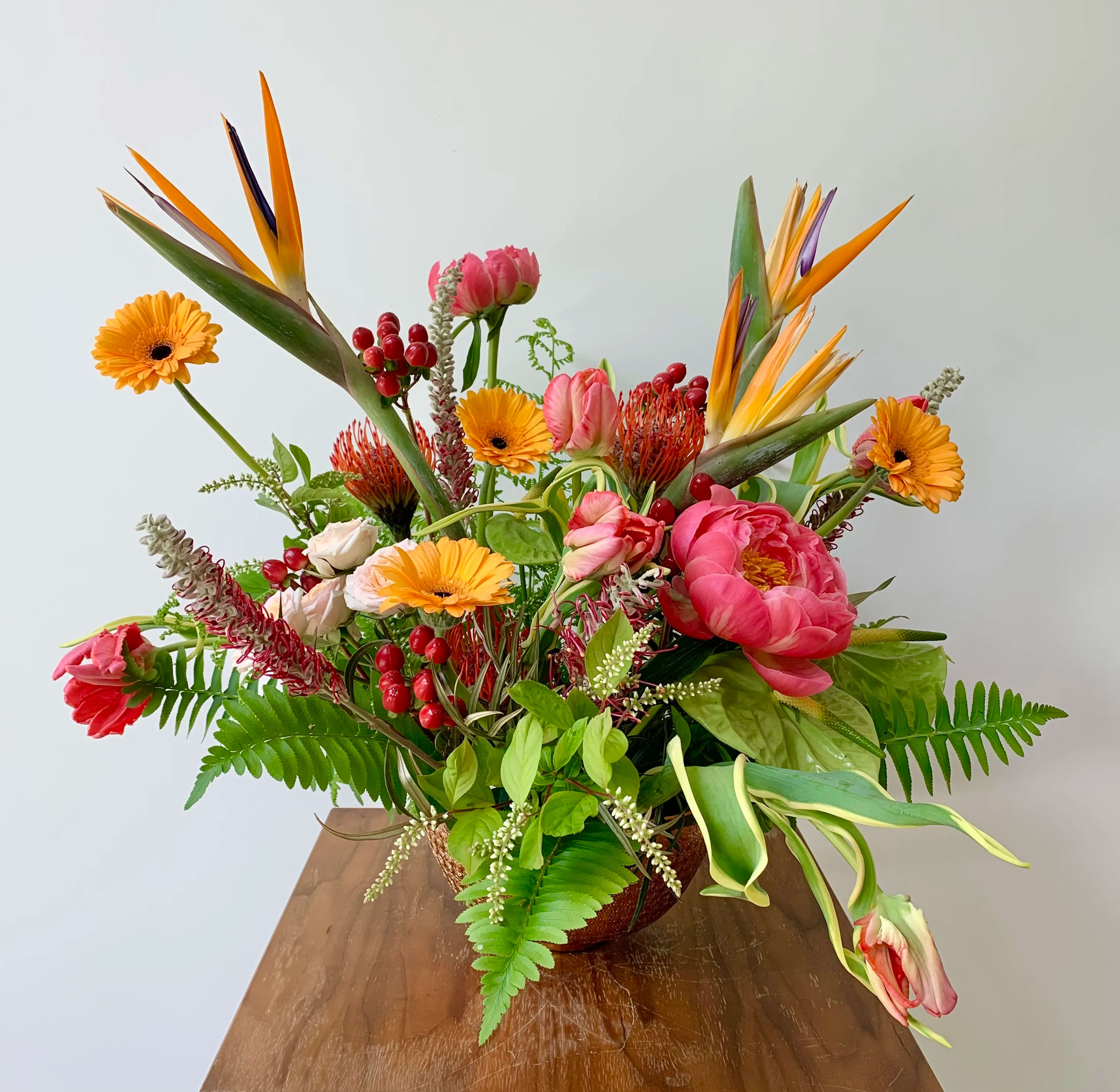 Tropical bouquet with pink peonies, orange gerbera daisies, and bird of paradise in a vase