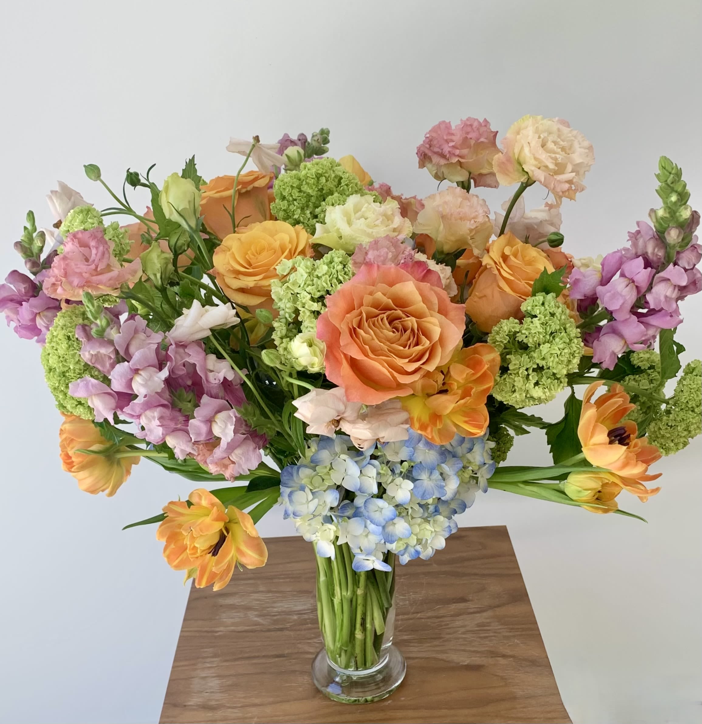 Citrussy  - A lovely tall flower bouquet arranged in an elegant tall glass vase. The theme here is a citrusy color palette with focus on oranges, yellows and lime greens. The choice of premium flowers depends on the availability of seasonal flowers.