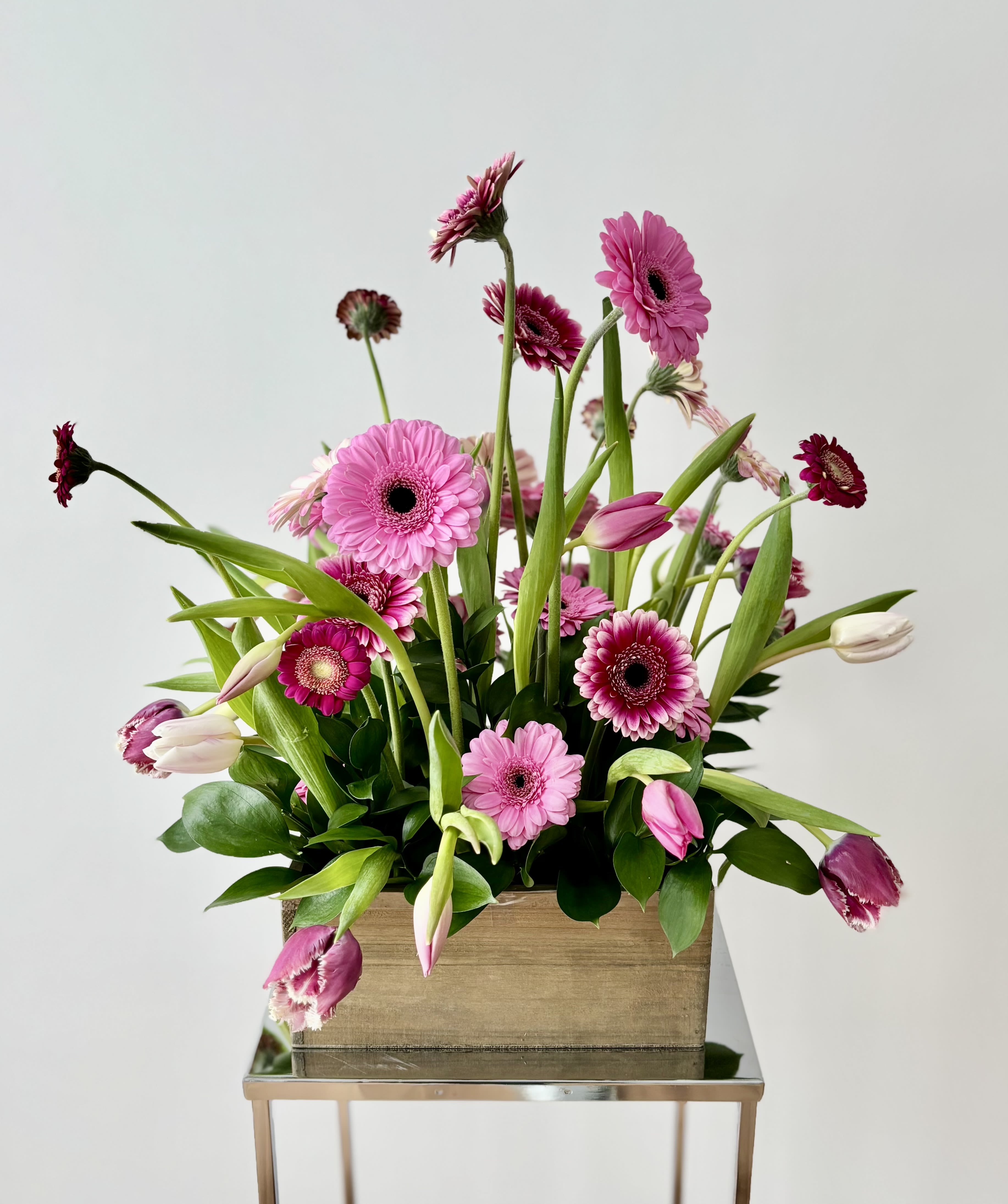 Pink gerbera daisies and tulips arranged in a wooden box
