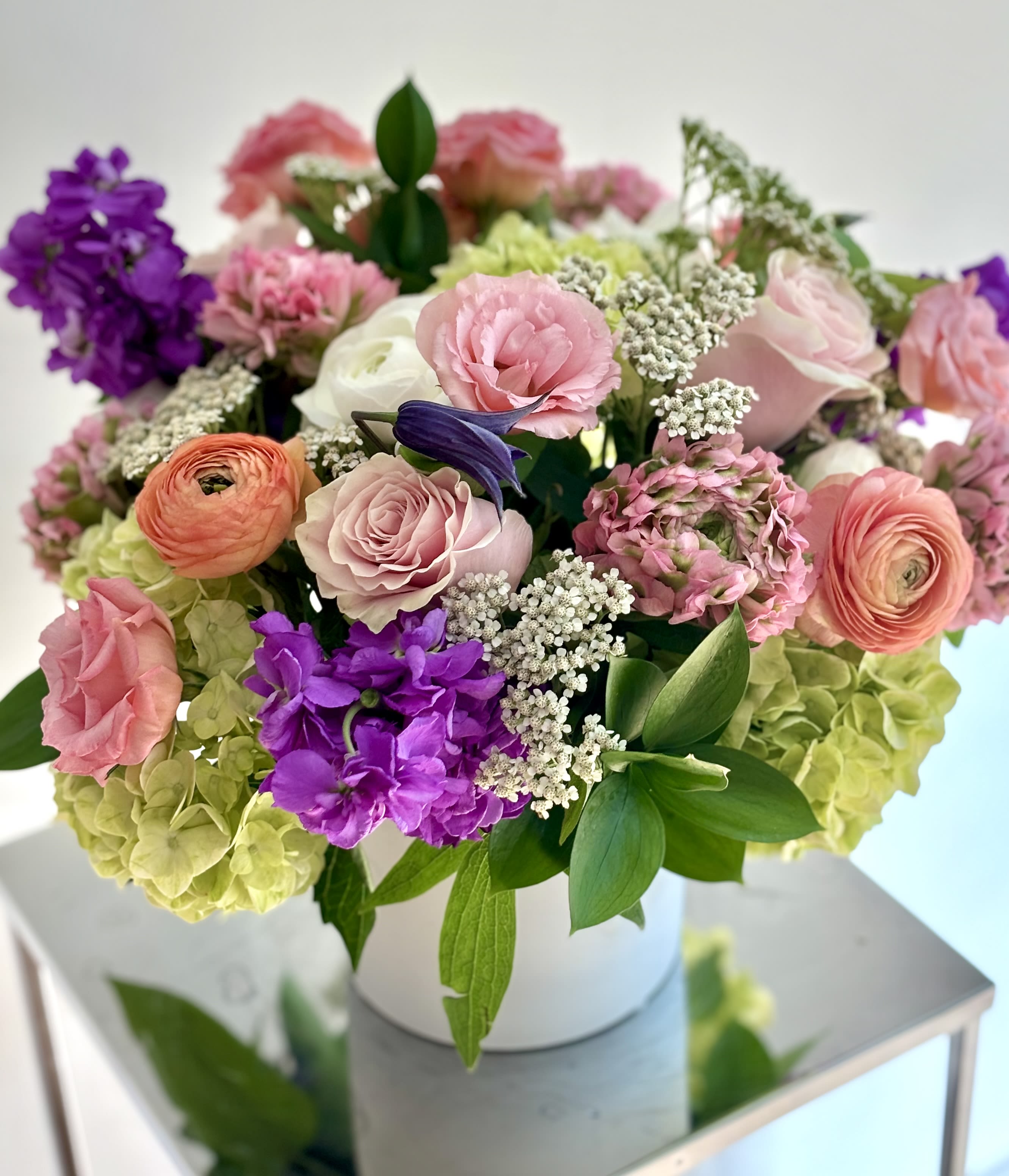 Mixed pink, purple, and green flowers arranged in a white box