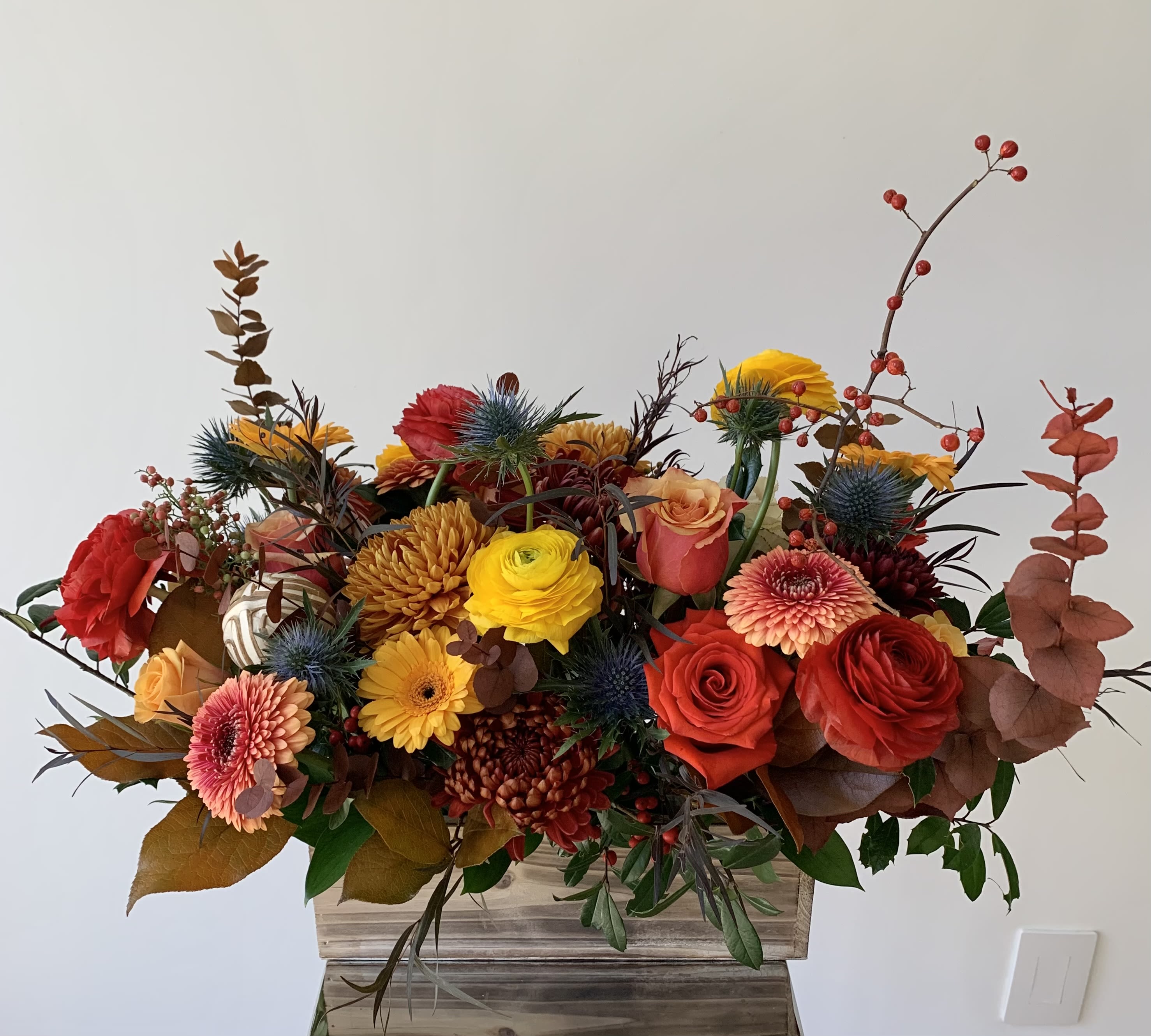 Mixed bouquet of red, yellow, and peach flowers in a wooden container