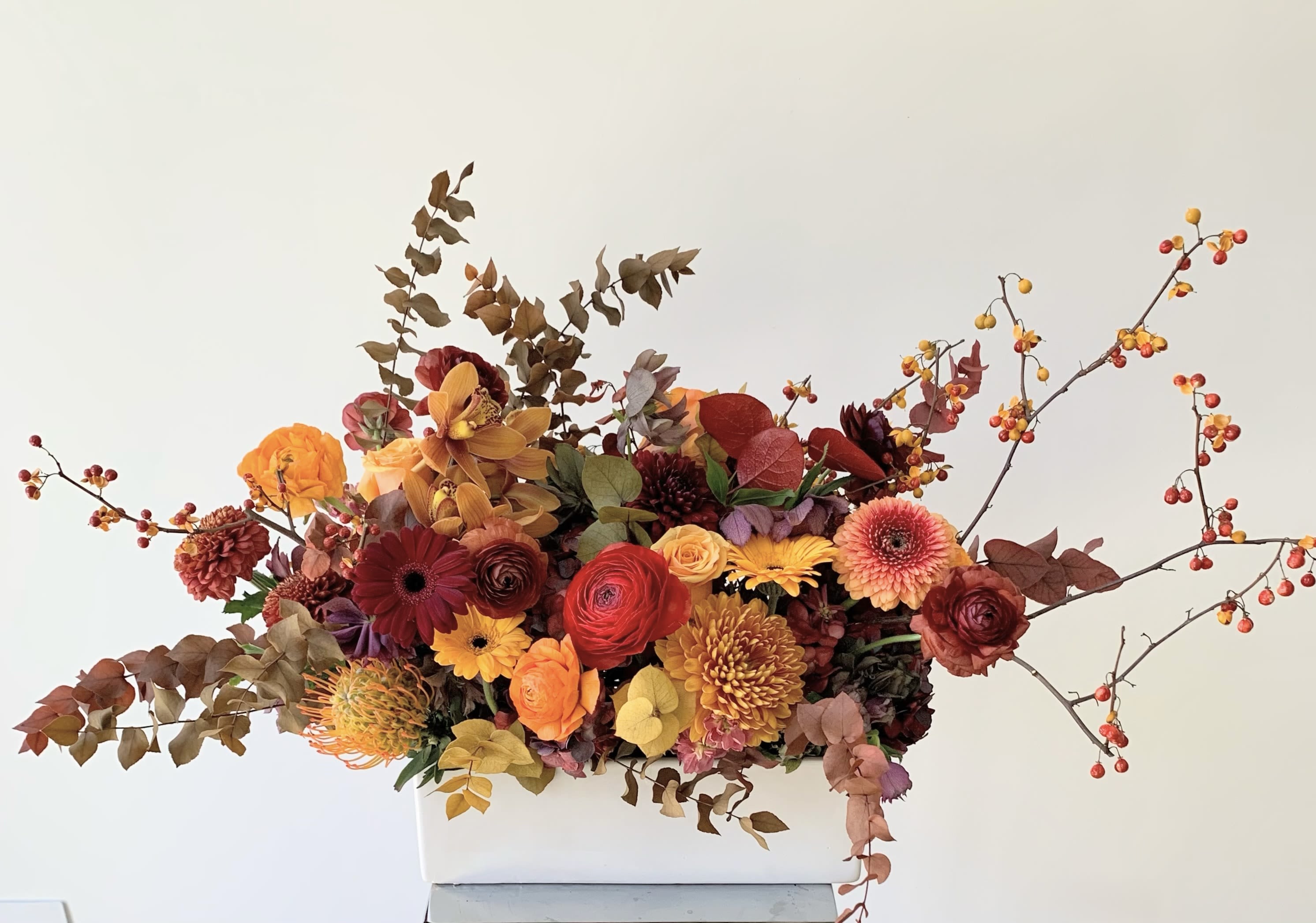 Autumn floral arrangement in a white rectangular vase with orange, red, and yellow blooms