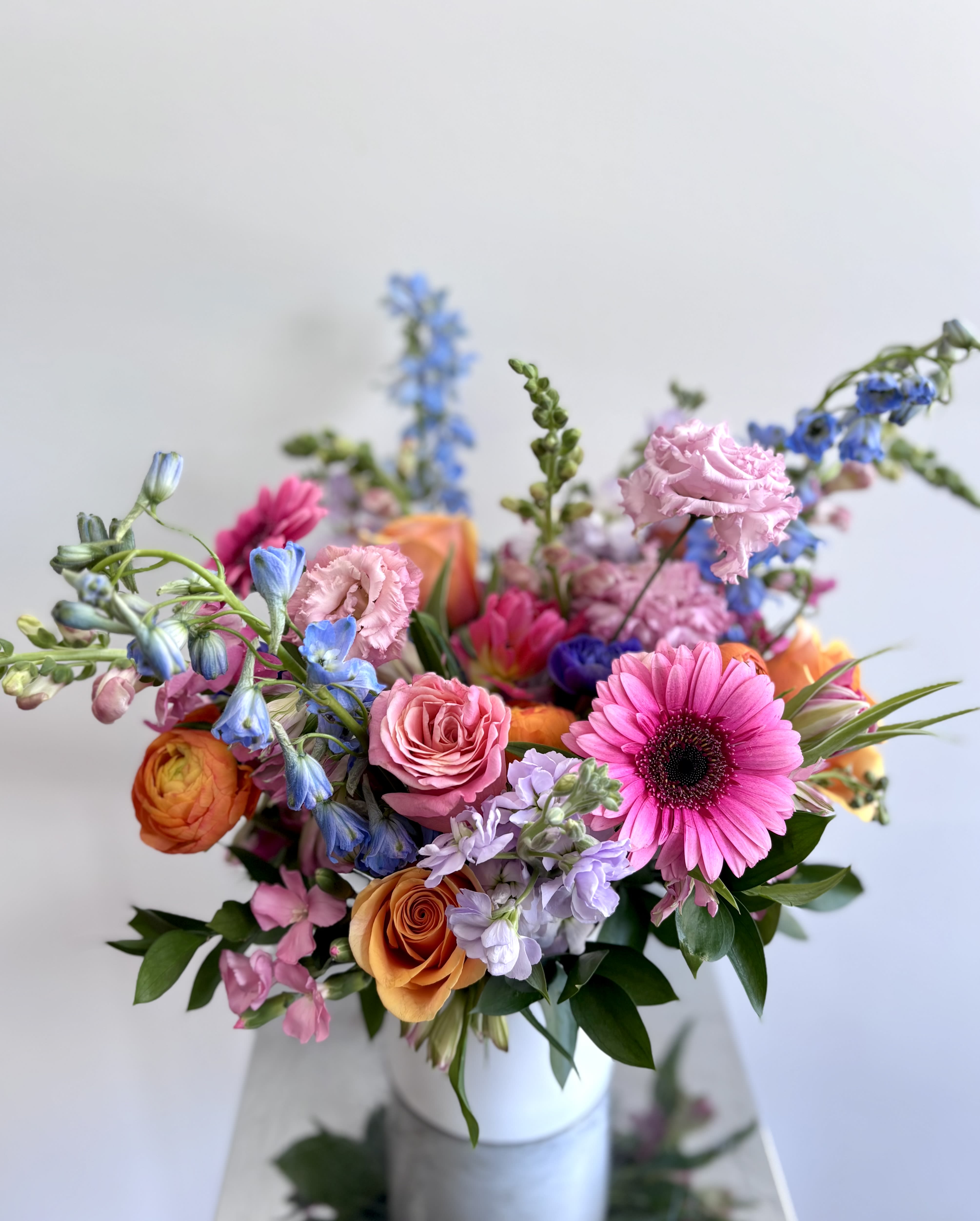 Colorful mixed bouquet in a white vase with pink, orange, blue, and purple blooms