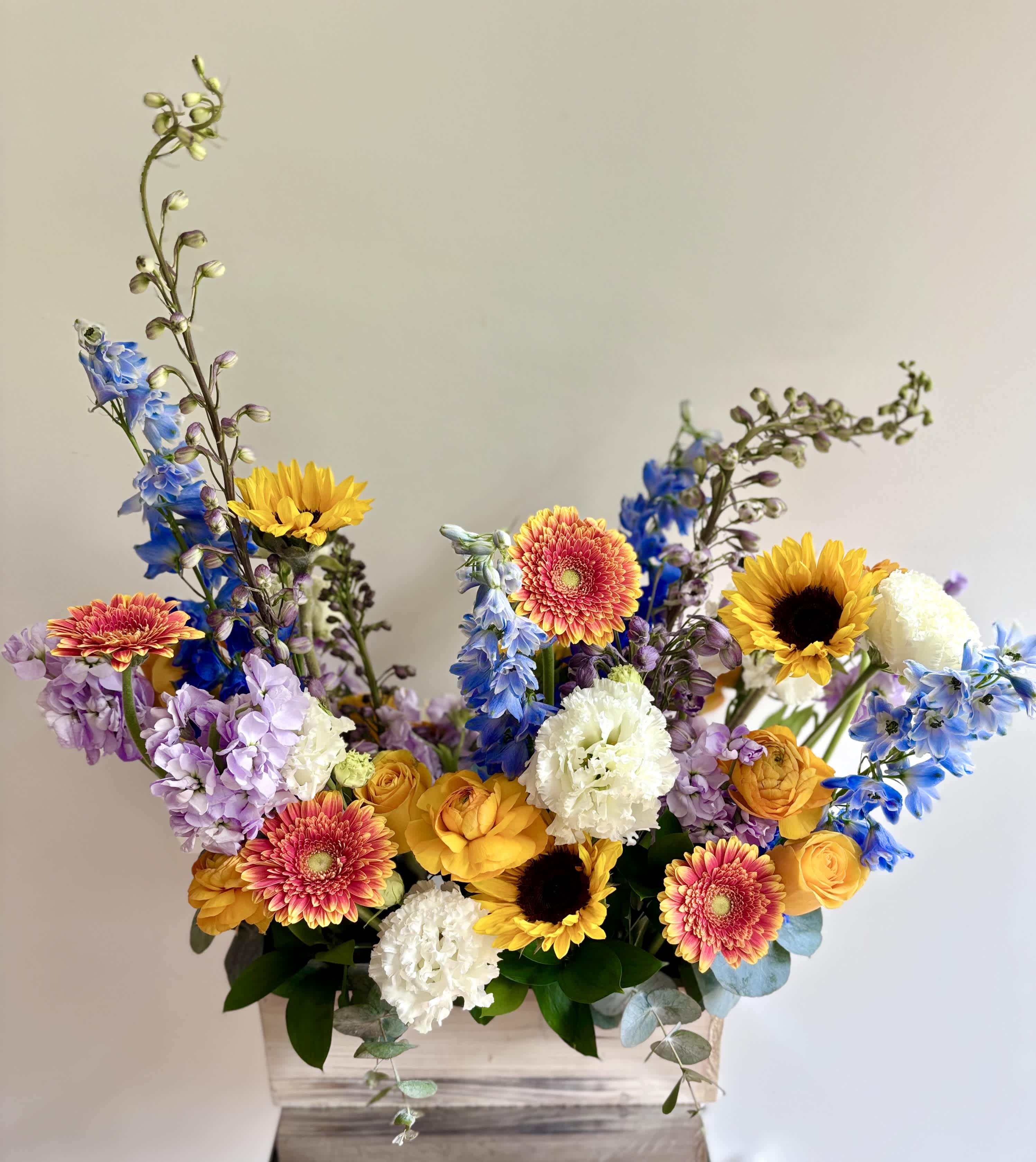 Mixed bouquet in a wooden box with sunflowers, gerbera daisies, and blue flowers