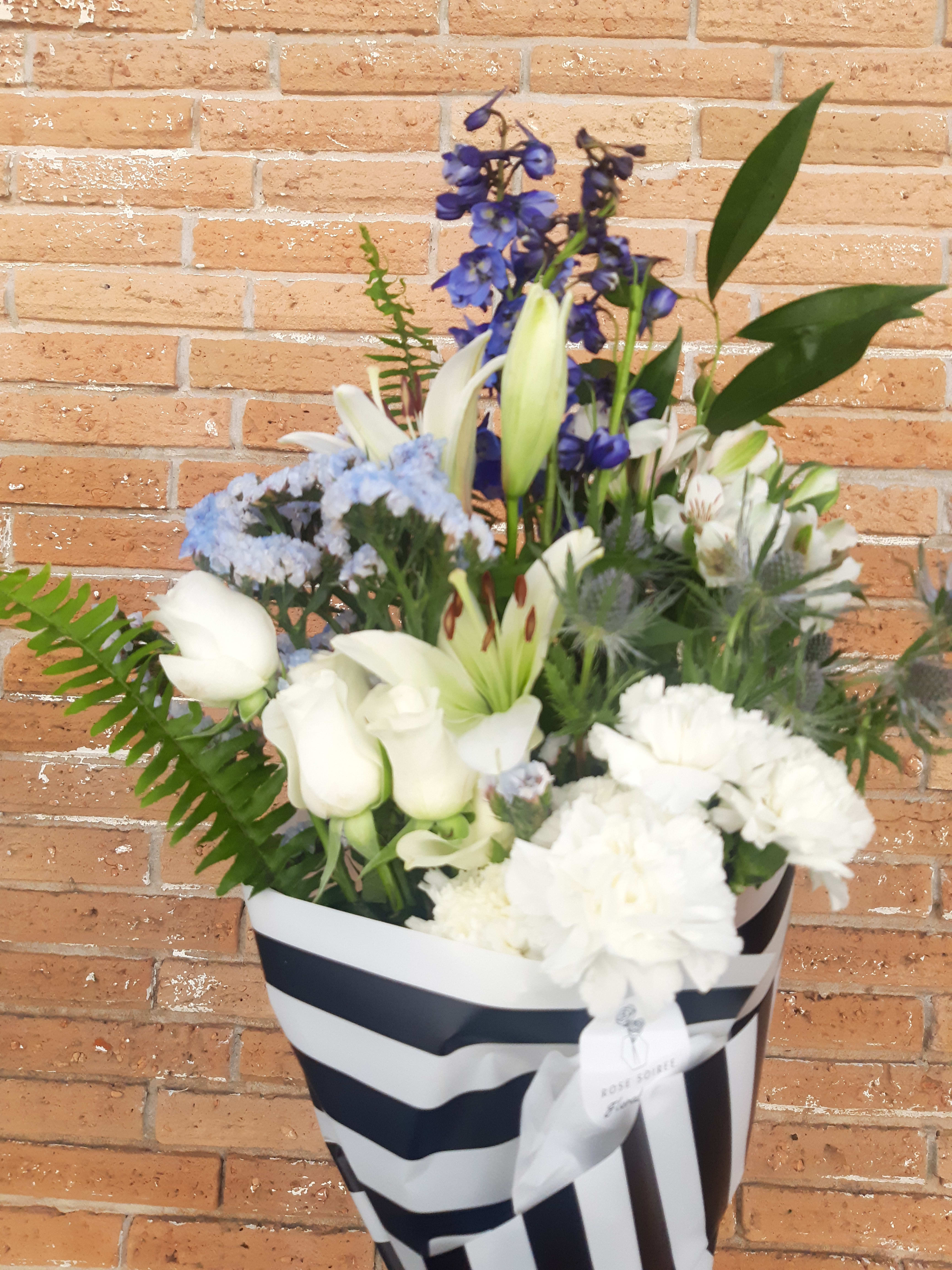 White lilies and carnations in a striped gift box with blue flowers