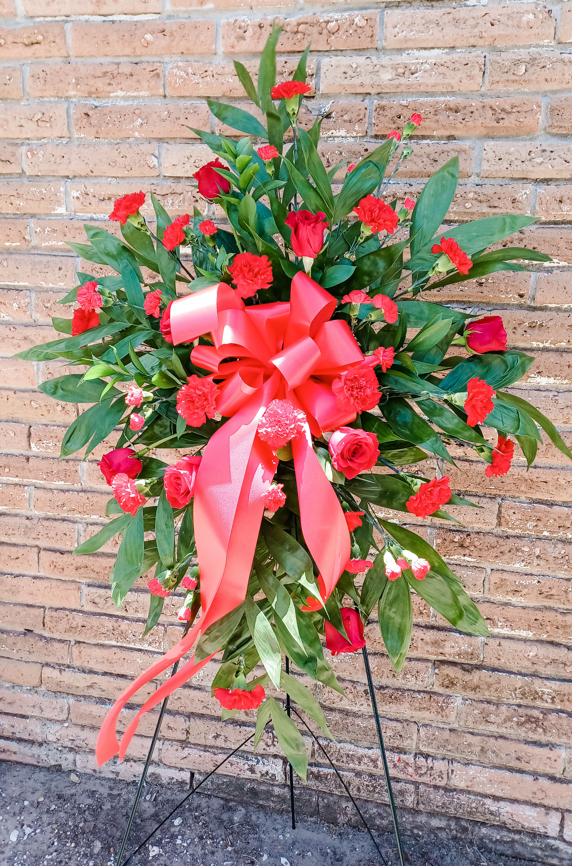 Standing floral spray with red roses and carnations, tied with a large red ribbon