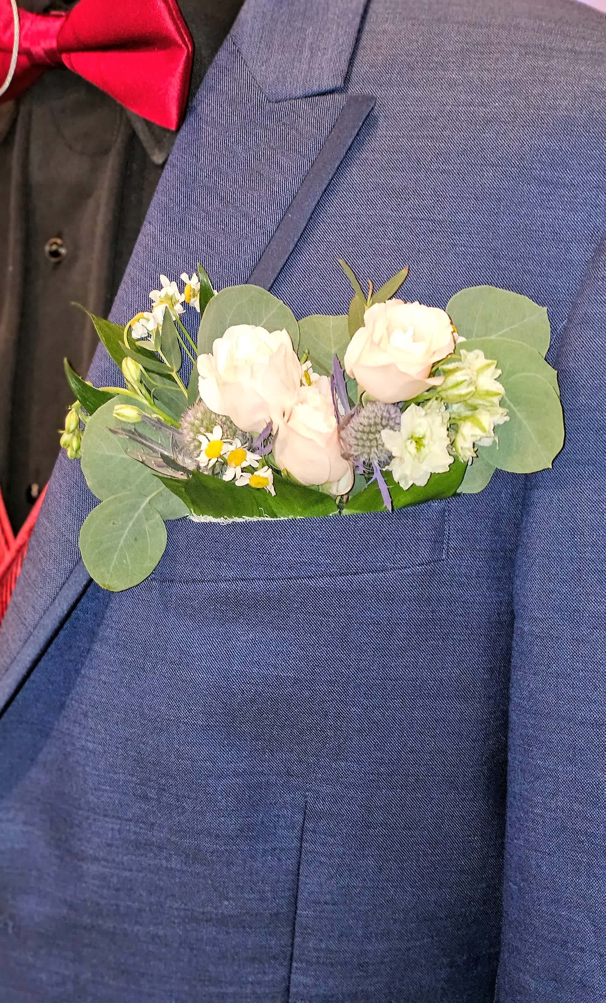 Boutonniere with pale roses and small white flowers on a blue suit jacket
