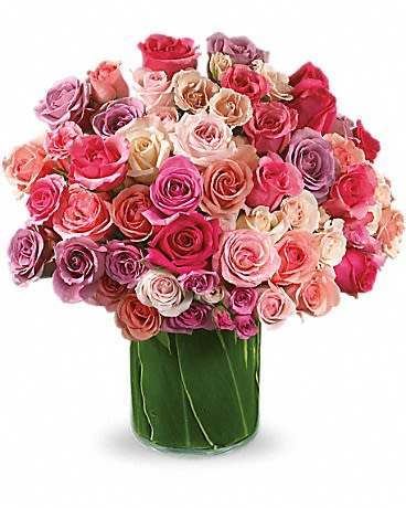 Large mixed pink and lavender rose arrangement in a glass vase lined with green leaves