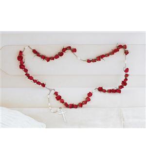 Red rose garland draped across a white headboard with a small cross pendant