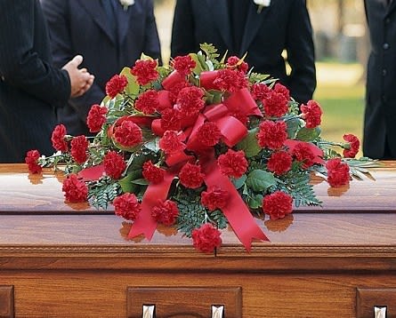 Red carnation casket spray with ribbon on a wooden casket