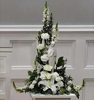 Tall white floral arrangement with lilies and roses around a statue