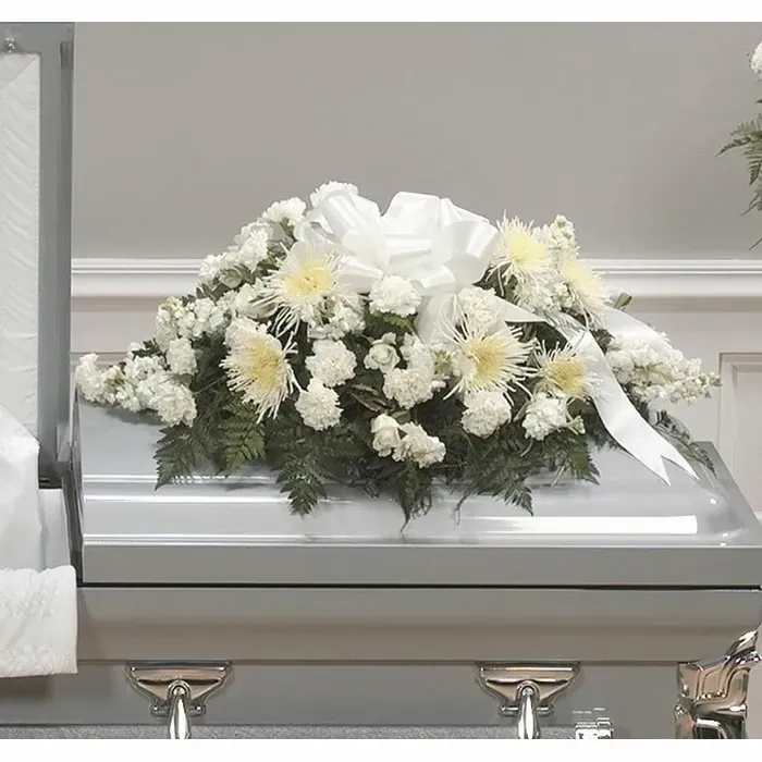 White floral casket spray with a large ribbon on a silver casket