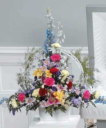 Tall mixed floral arrangement in a white container with bright multicolored blooms