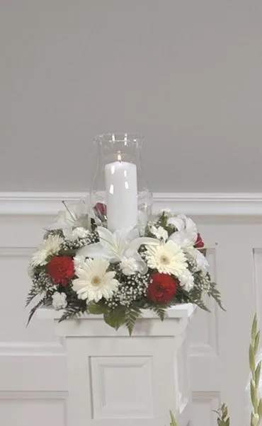 White candle in a glass hurricane surrounded by red and white flowers