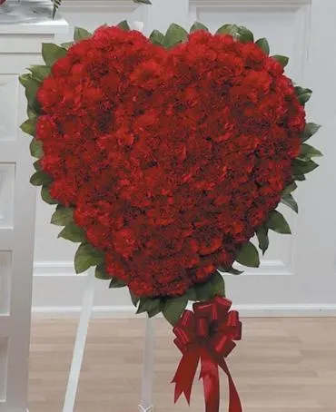 Heart-shaped red floral arrangement on a white stand with a red ribbon