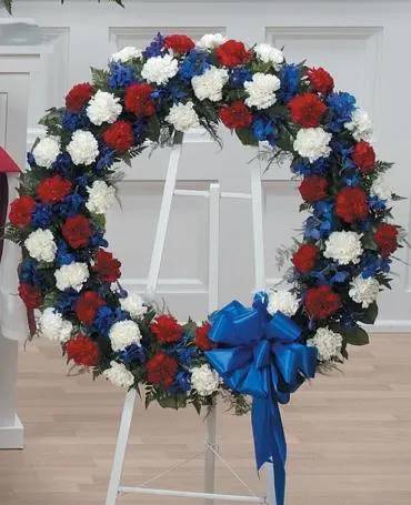 Heart-shaped floral wreath with red, white, and blue flowers on a stand