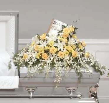 Yellow and white floral casket spray on a gray casket