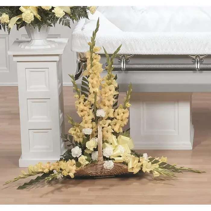 Yellow floral funeral spray on a wicker base beside a casket