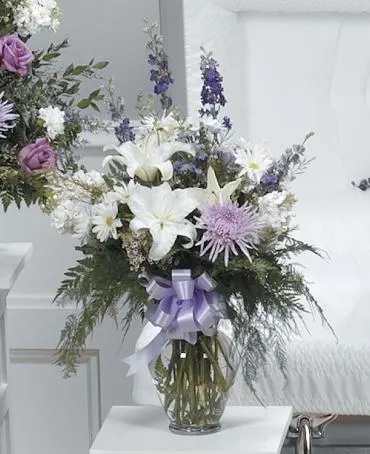 White and lavender floral arrangement in a glass vase with a ribbon
