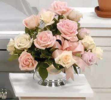 Pink and white roses arranged in a clear glass vase with a pink ribbon