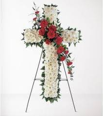 Cross-shaped floral funeral spray with white flowers and red roses on a stand