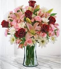 Bouquet of red roses, pink lilies, and white daisies in a glass vase