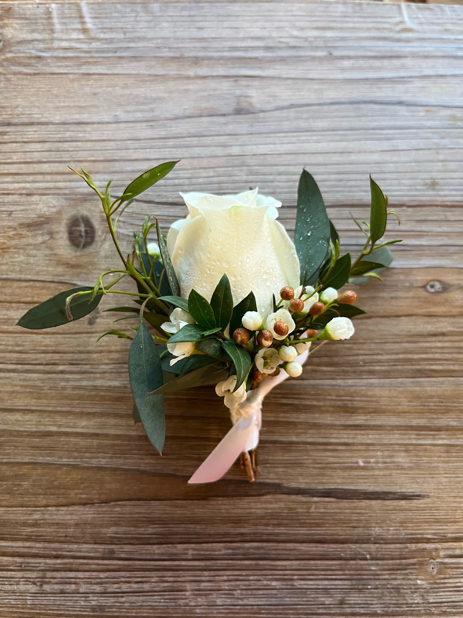 White rose boutonniere with greenery and small white berries