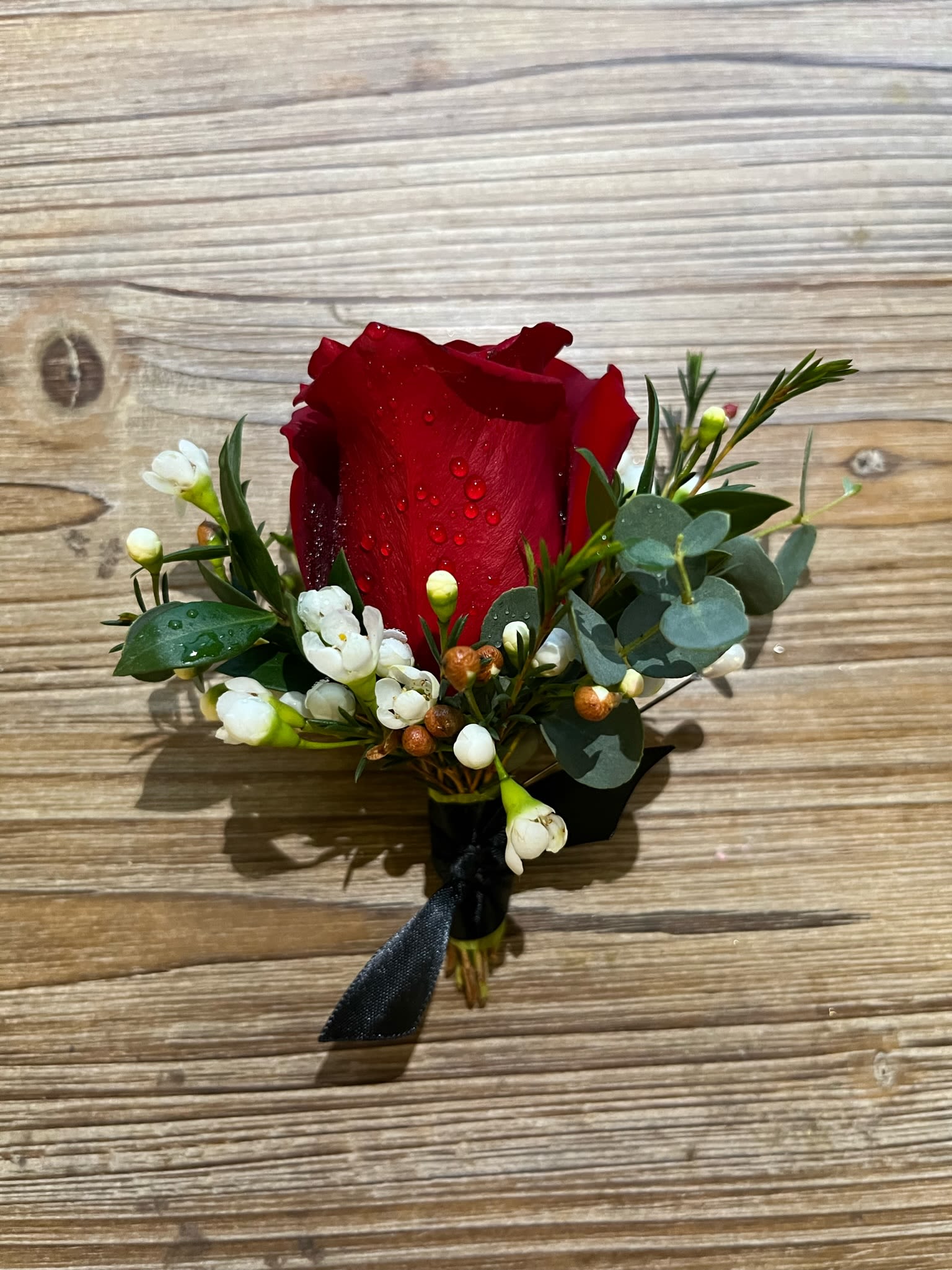 Red rose boutonniere with white waxflowers and eucalyptus