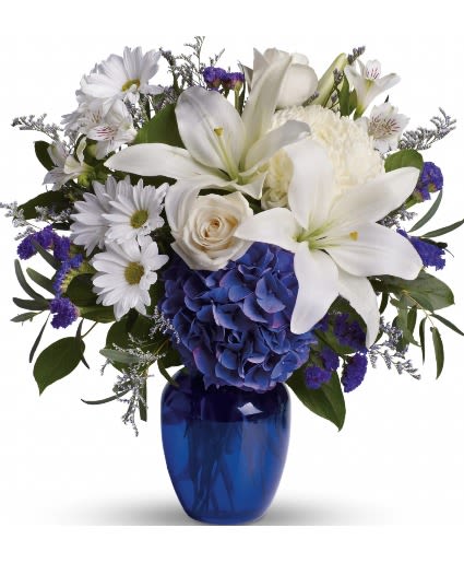 White lilies and daisies with blue hydrangea in a cobalt vase