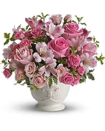 Pink roses and lilies arranged in a white pedestal vase