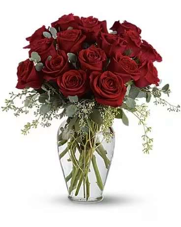 Red roses arranged in a clear glass vase with trailing greenery