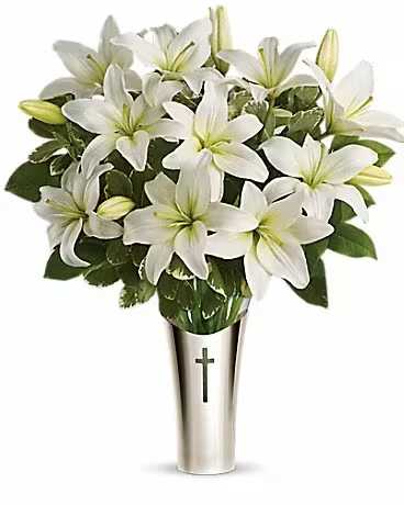 White lilies arranged in a silver vase with a cross emblem