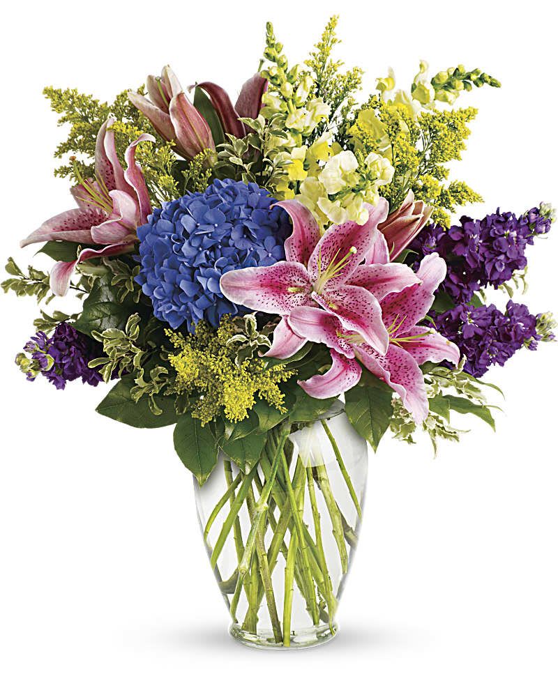 Bouquet of pink lilies, blue hydrangea, and purple flowers in a glass vase