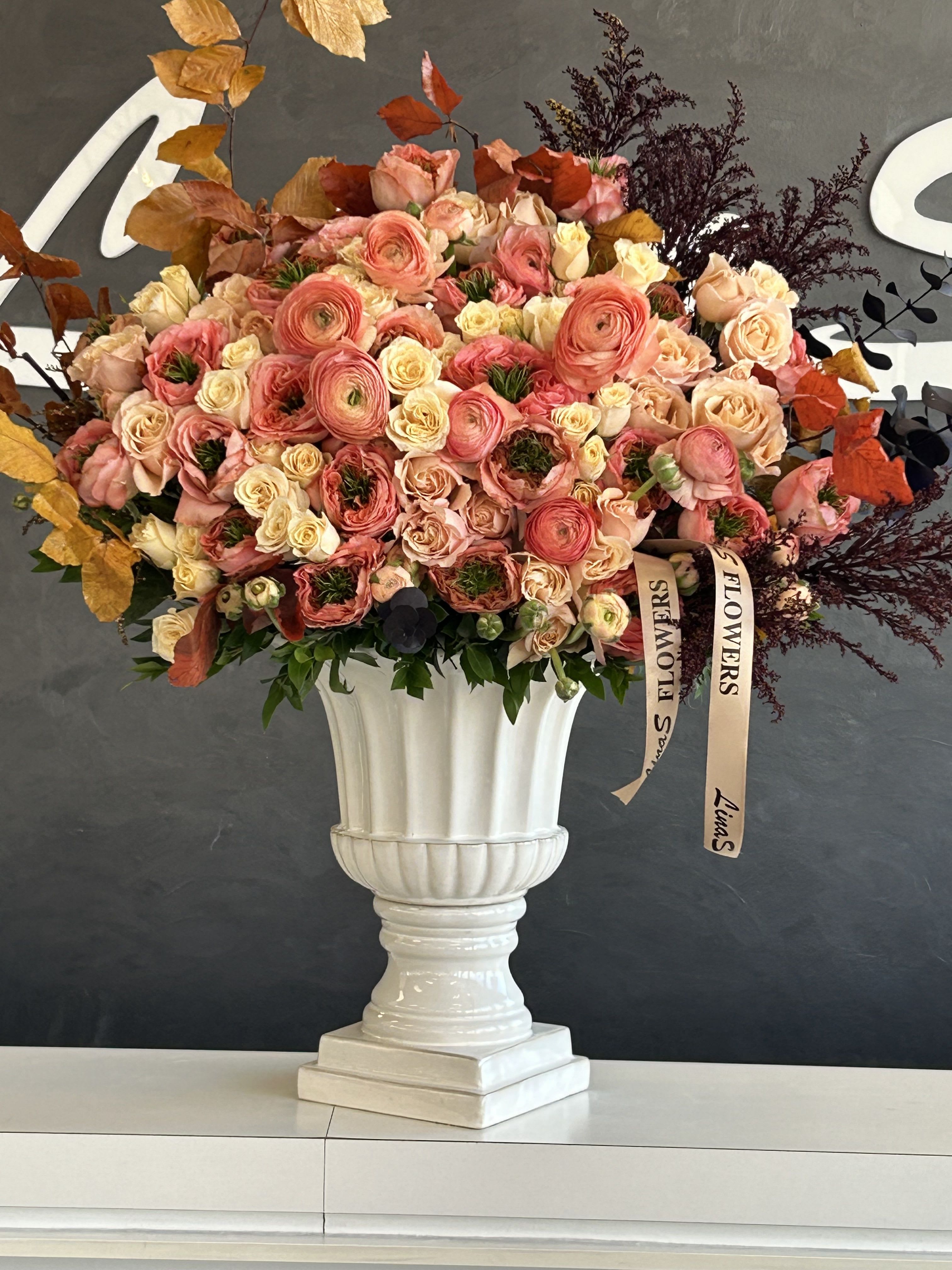 Large pink and peach rose arrangement in a white pedestal vase