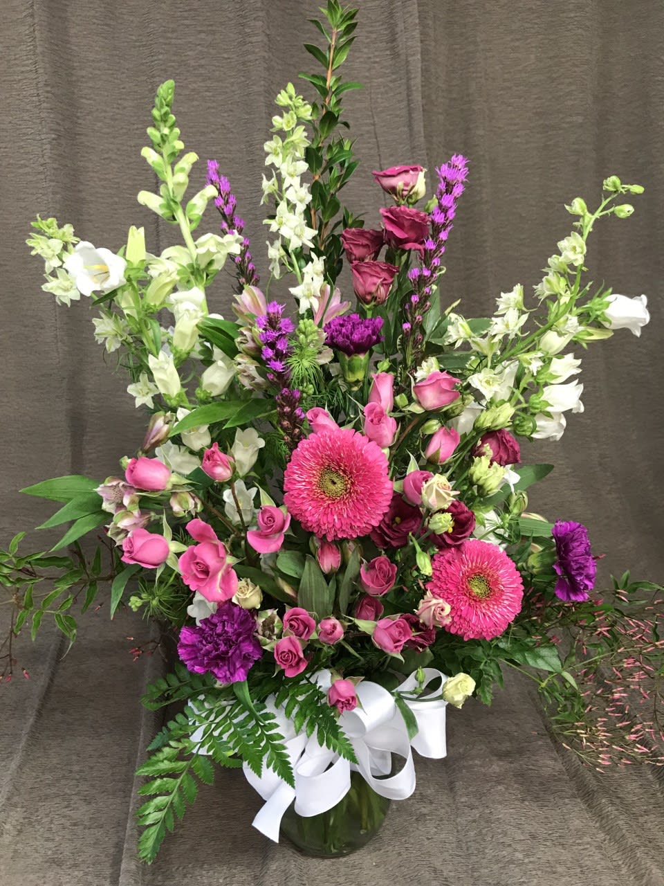 Pink and white mixed flower arrangement in a glass vase with a white ribbon