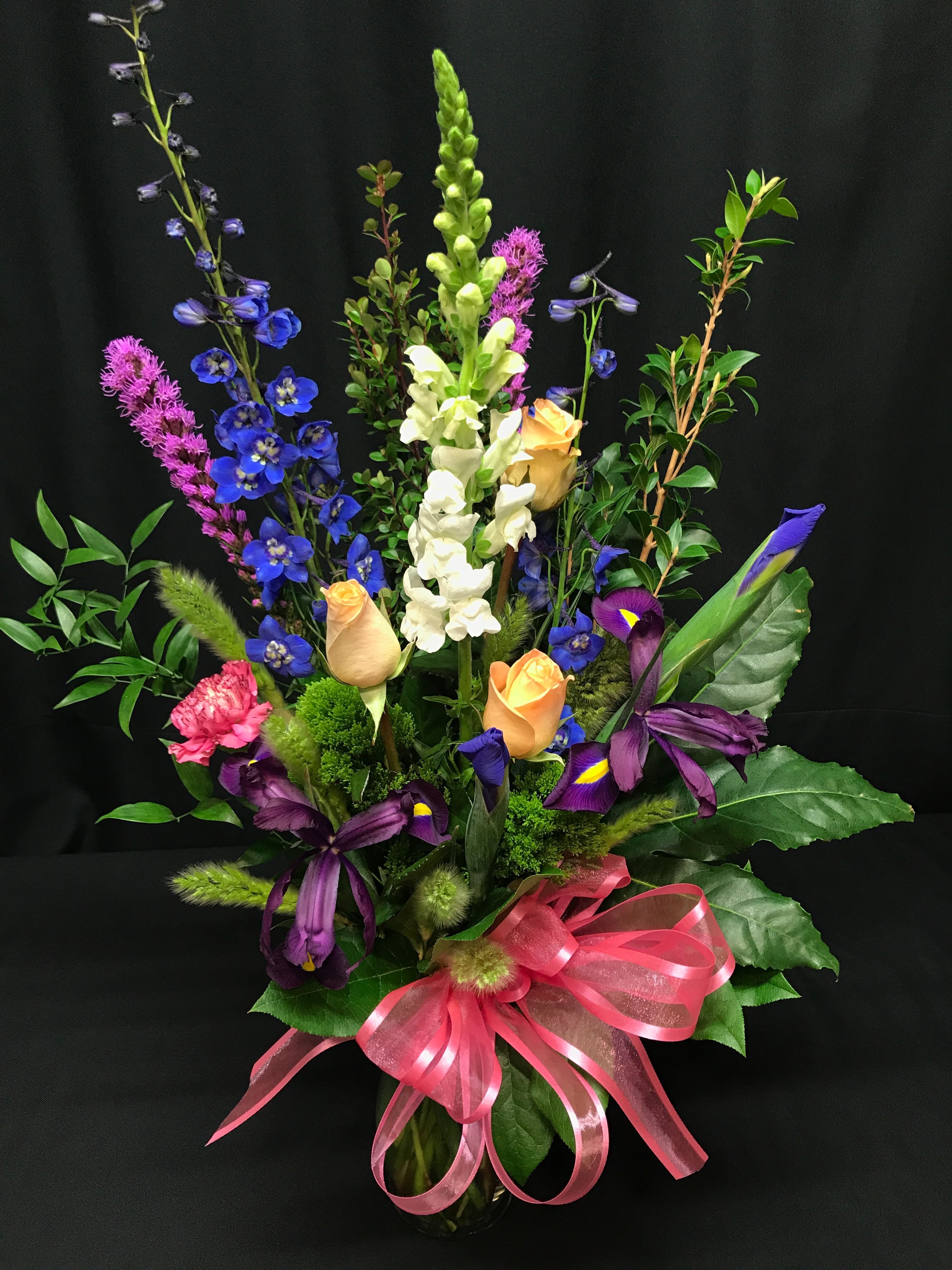 Tall mixed bouquet with blue, white, purple, and peach flowers in a glass vase